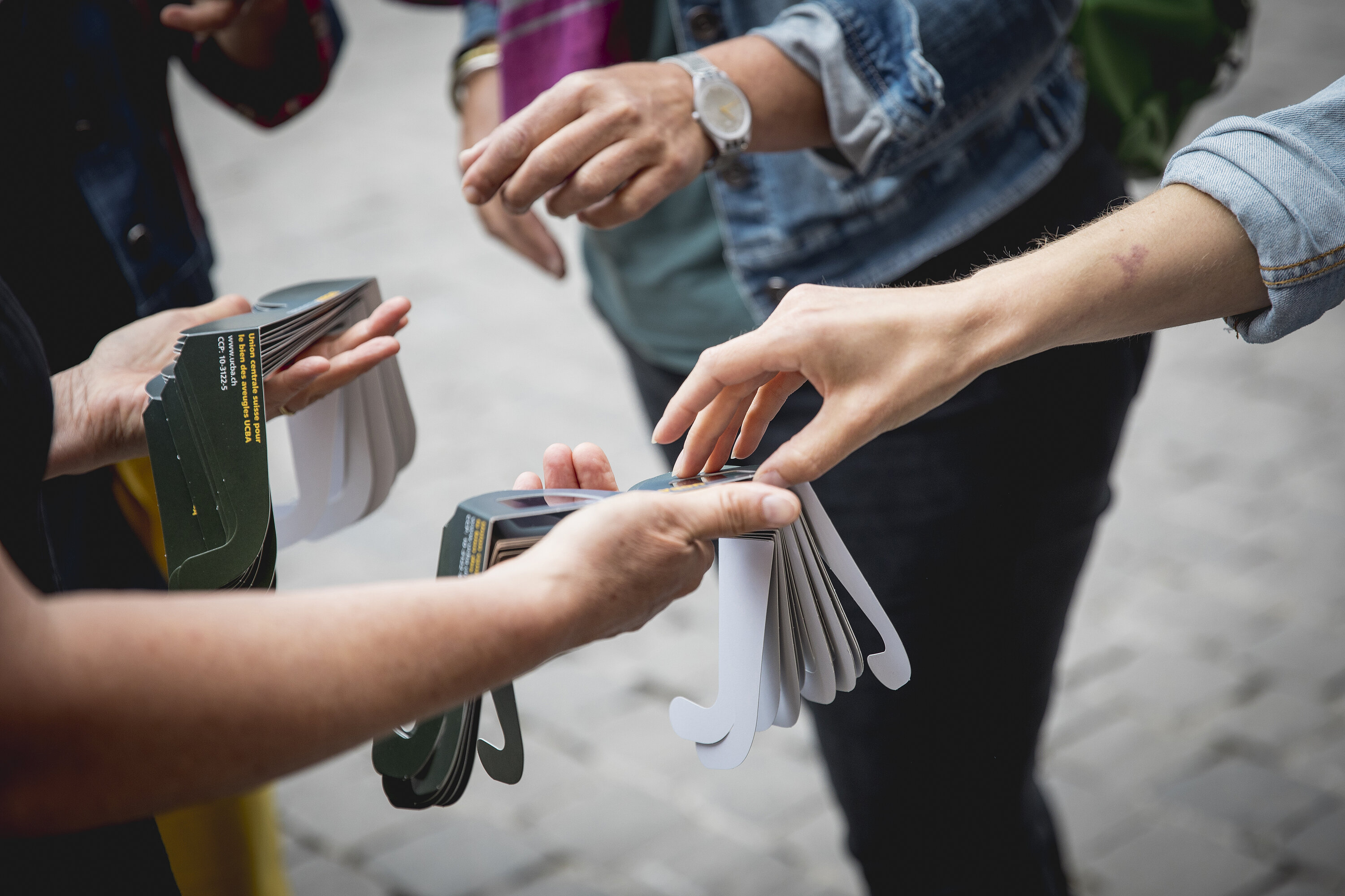 Deux mains tendent des lunettes de simulation d’une déficience visuelle aux participantes et participants à la formation à la chaîne de l’accessibilité lors du projet pilote Yverdon culture accessible, ©Yverdon-les-Bains/ Zoé Jobin, 2022